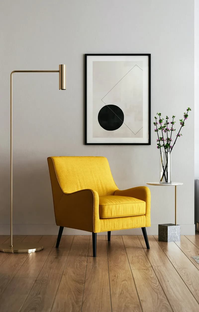 Mustard-yellow armchair beside a brass floor lamp, with a framed abstract print above a pale wall