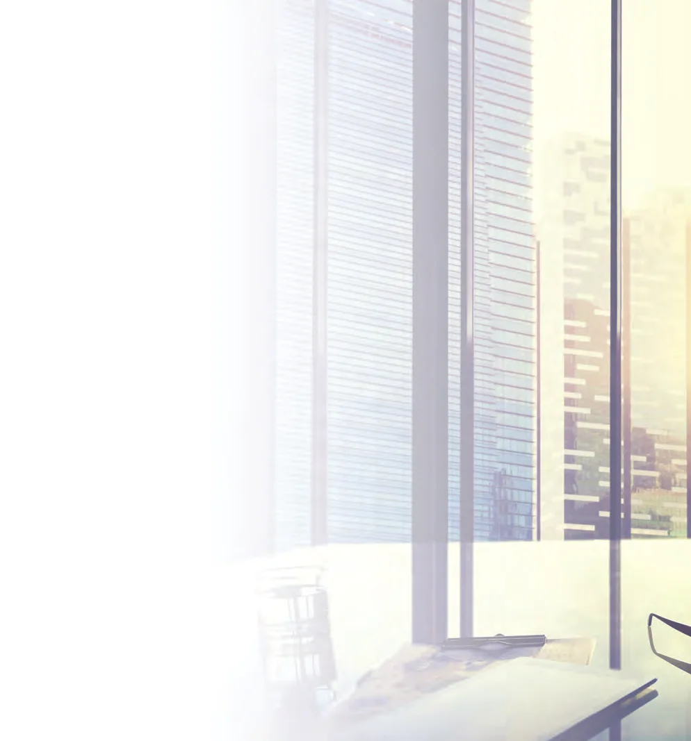 Sunlit office window with venetian blinds, city towers beyond, and a desk edge holding drawings and a pair of glasses